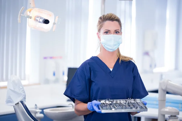 Dentist in mask holding tray of tools