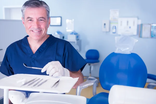 Dentist in blue scrubs holding tools