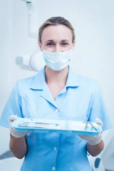 Female dentist in surgical mask holding tray of tools