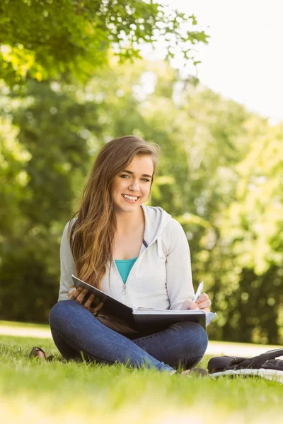 Smiling university student sitting and writing on notepad