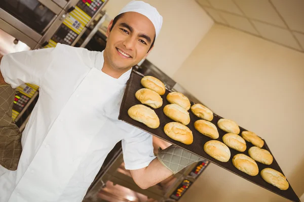 Baker smiling at camera holding tray of rolls