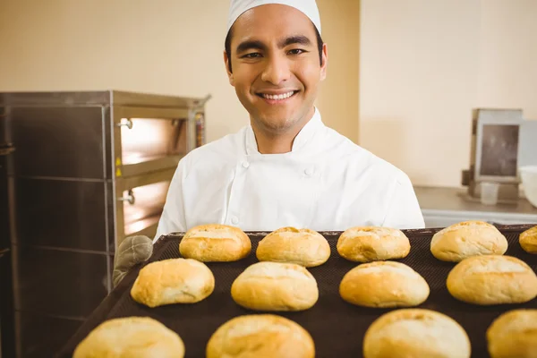 Baker smiling at camera holding tray of rolls