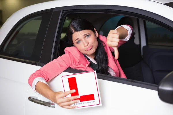 Woman gesturing thumbs down holding a learner driver sign