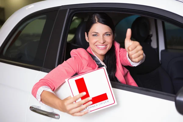 Woman gesturing thumbs up holding a learner driver sign