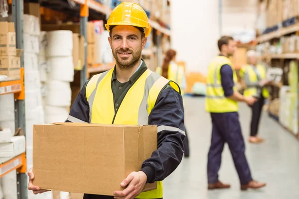 Warehouse worker smiling at camera carrying a box