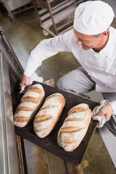 Baker taking tray of bread out of oven