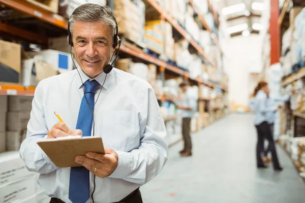 Smiling warehouse manager writing on clipboard