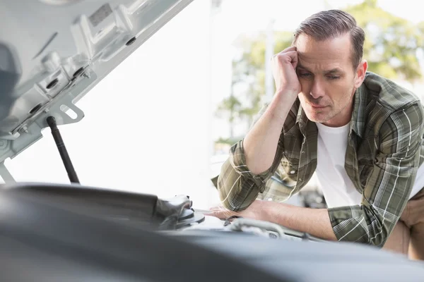 Upset man checking his car engine after breaking down