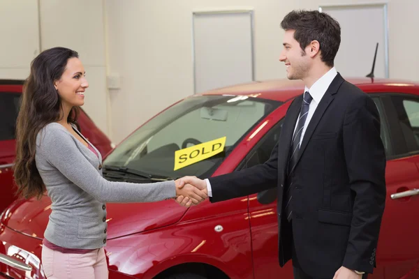 Persons shaking hands in front of sold car