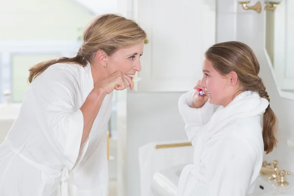 Happy mother and daughter brushing teeth together