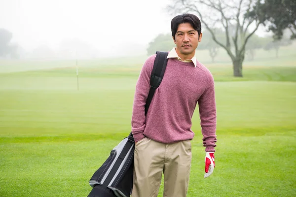 Golfer standing holding his golf bag