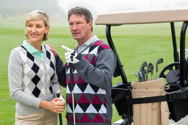 Golfing couple with golf buggy behind