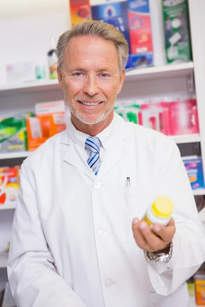 Smiling senior pharmacist holding medicine jar