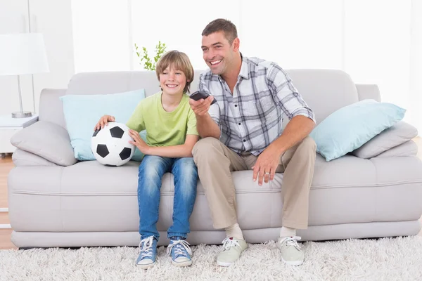 Father and son watching soccer match on sofa