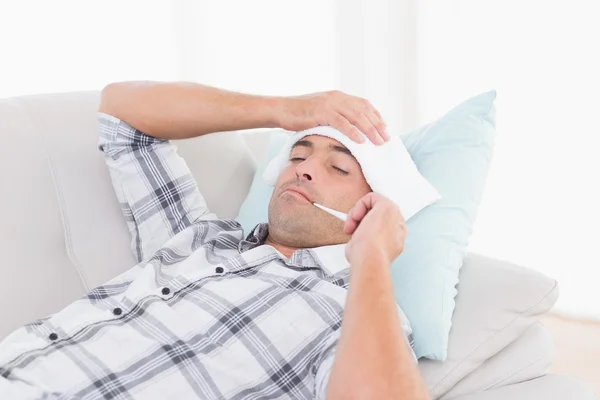 Man measuring temperature on thermometer on sofa