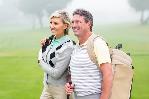 Golfing couple smiling and holding clubs