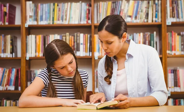 Teacher and girl reading book in library