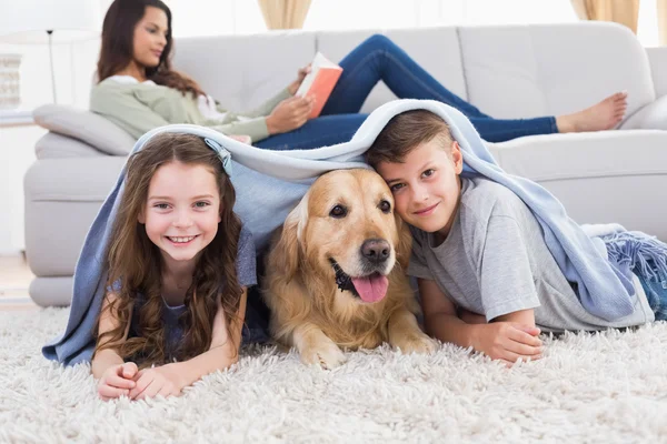 Happy siblings with dog under blanket