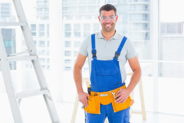 Smiling repairman in overalls at bright office