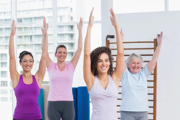 Female friends with arms raised exercising in gym