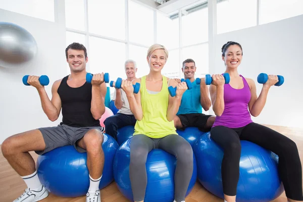 People sitting on balls and lifting weights in fitness club
