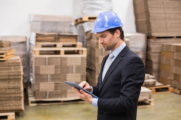 Warehouse manager wearing hard hat using tablet