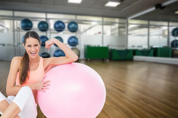 Fit woman flexing muscles by fitness ball