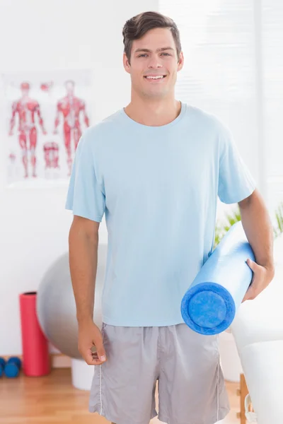 Happy young man holding exercise mat