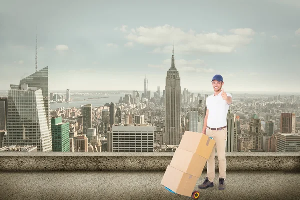Composite image of happy delivery man pushing trolley of boxes