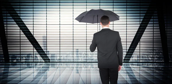Composite image of businessman sheltering under black umbrella