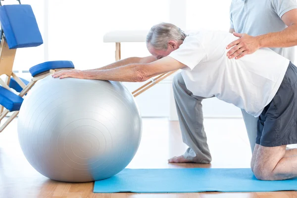 Physiotherapist helping man with exercise ball