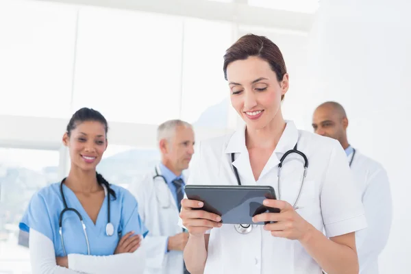 Confident female doctor holding tablet with her team behind