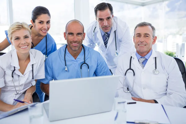 Happy team of doctors looking at camera in behind laptop compute