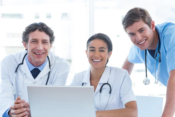 Team of doctors working on laptop and smiling at camera