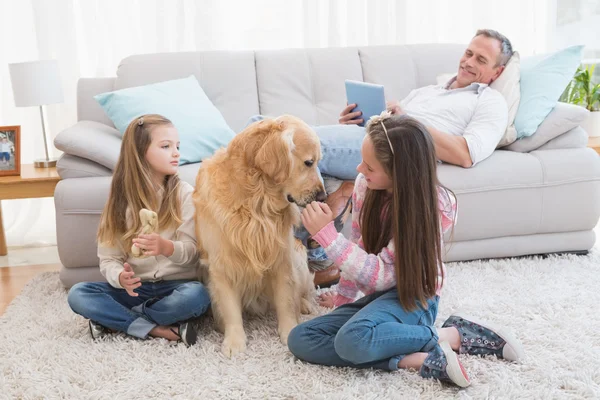 Sisters petting golden retriever on rug