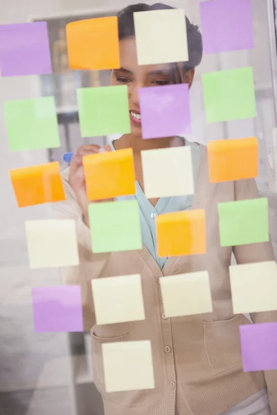 Businesswoman writing on sticky notes on window