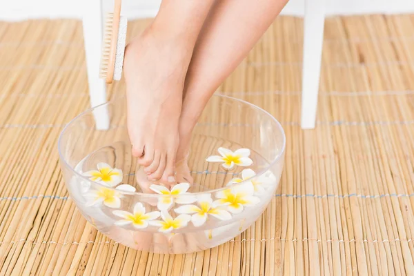 Woman washing her feet in a bowl of flowers