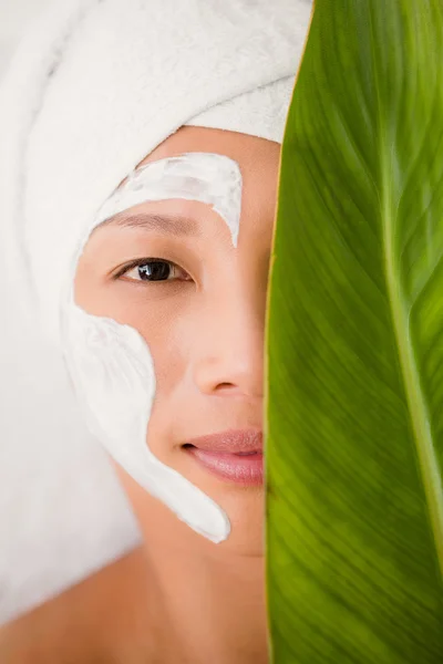 Woman with cream treatment behind leaf