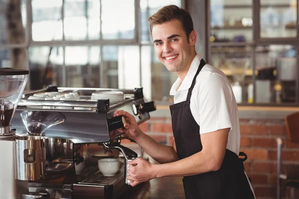 Smiling barista steaming milk at coffee machine