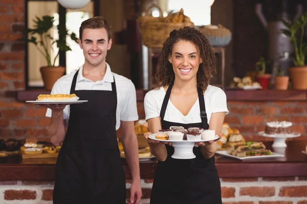 Smiling waiter and waitress showing plates with treat