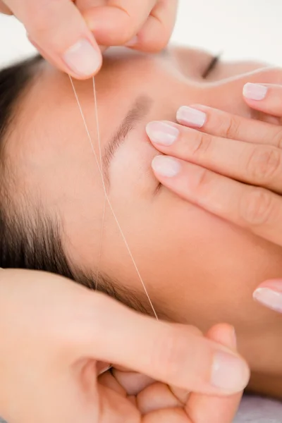 Hands threading beautiful woman's eyebrow