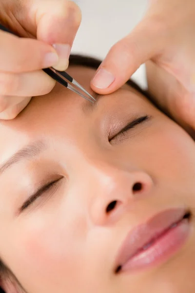 Woman using tweezers on patient eyebrow