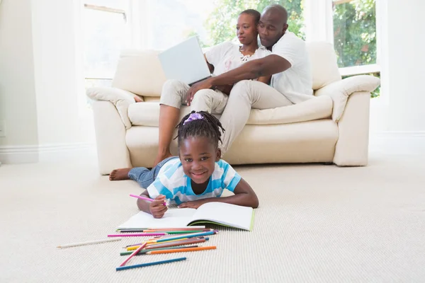 Pretty couple using laptop on couch and their daughter drawing