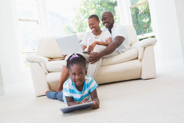 Pretty couple using laptop on couch and their daughter using tab