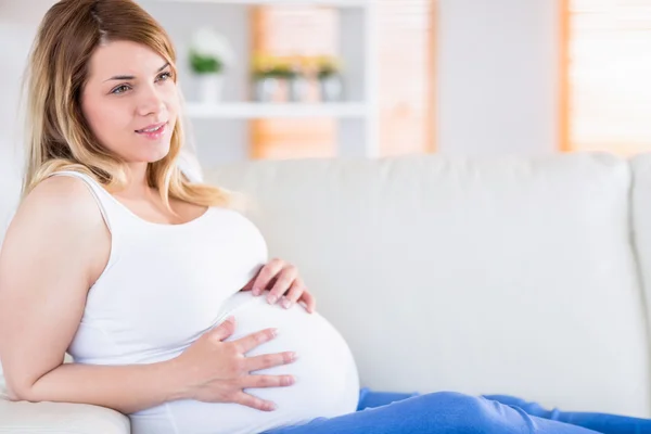 Pregnant woman touching her belly on the couch