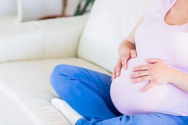 Pregnant woman sitting on couch touching her belly