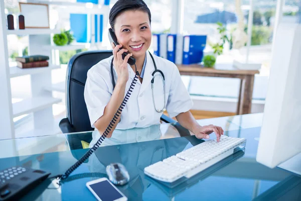 Smiling doctor having phone call and using her computer