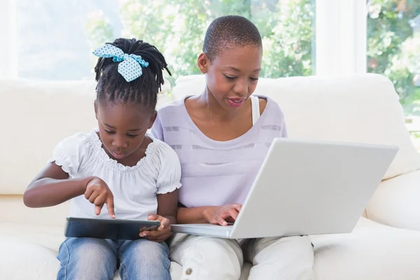 Happy smiling mother using laptop with her daughter using tablet