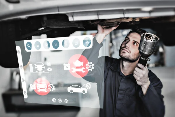 Mechanic examining under the car with torch