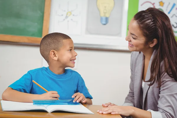 Pretty teacher helping pupil at desk